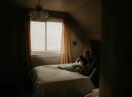 Young couple laying on bed with their newborn baby.