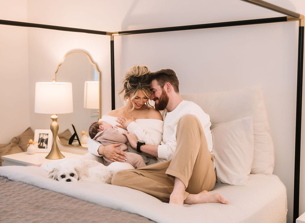 New parents snuggling on their bed with their new baby and puppy.