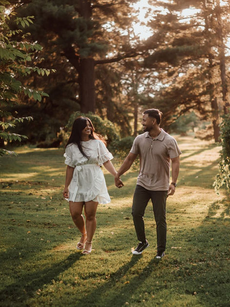 Candid engagement photo of a couple walking hand-in-hand through a sun-drenched Ottawa park during golden hour.