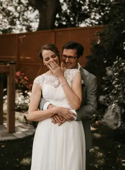 A bride laughing while being cuddled by her husband.