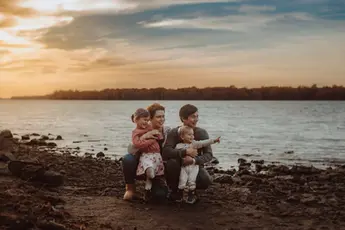 A young family sits by the Ottawa River during a their beautiful outdoor family lifestyle session in Ottawa, Ontario, during sunset.