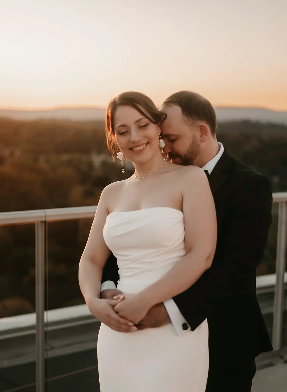 A bride is snuggled by her husband after their intimate Ottawa wedding, with a beautiful sunset in the back.