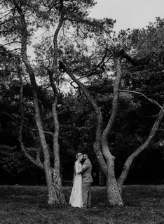 Black and white image of bride and groom embracing between two tall trees.