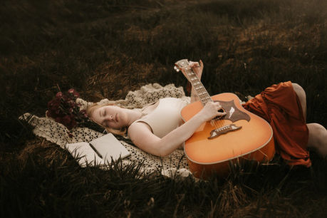 A young woman laying in the grass stumming her guitar.