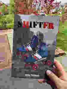 Holding a paperback book with a pair of rollerskates on the cover. Title reads: SHIFTER Author reads: Willy Yonkers.