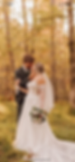 Bride and groom embrace in a forest. Autumn leaves create a warm backdrop. Bride holds a bouquet; both appear joyful and intimate.