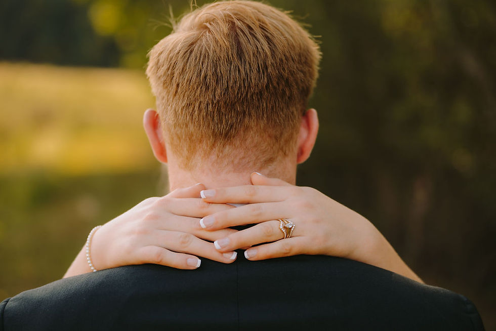 Person with short hair viewed from behind, embraced by hands with a ring. Soft focus background has greenery and tranquil atmosphere.