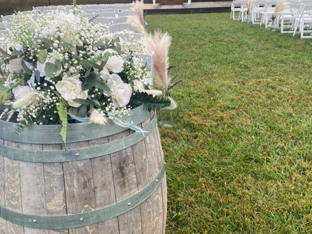 Elegant white and green silk florals on a hexagon arbor with glass jugs and pampas grass decorate the aisle