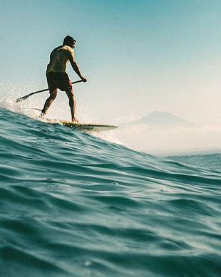 Paddle surfer in a wave, volcano in the background