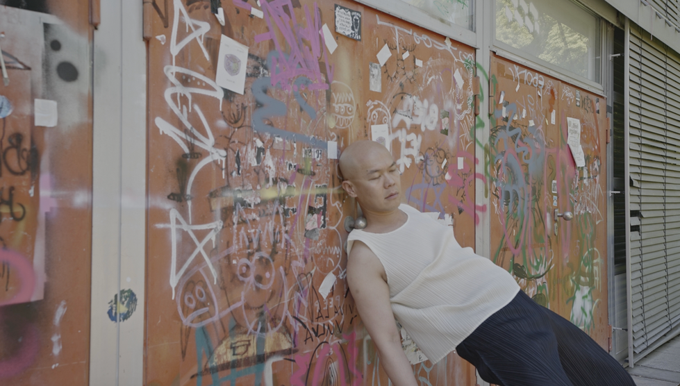 Performance documentation showing the artist leaning against a wall in a public space.
