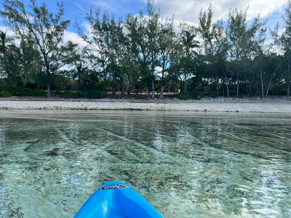 Photo taken from a kayak approaching a secluded beach in Eleuthera, Bahamas, with the kayak’s front point visible and surrounded by stunning, crystal-clear water.