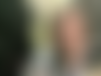 A woman smiles with three dogs in a wooded area. Two dogs have black and white fur, one is black. Sunlight filters through the trees.