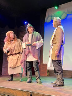a man with a crown on his head talks to two other men on a stage
