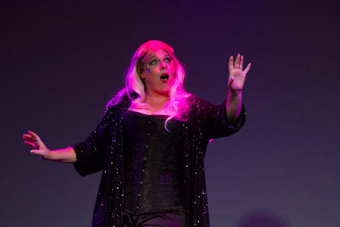 a woman in a pink wig and sequined jacket holds up her hand