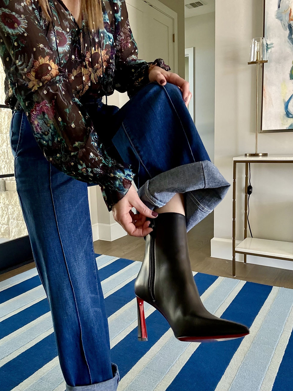 woman showing the zipper of her boot while wearing jeans and a blouse