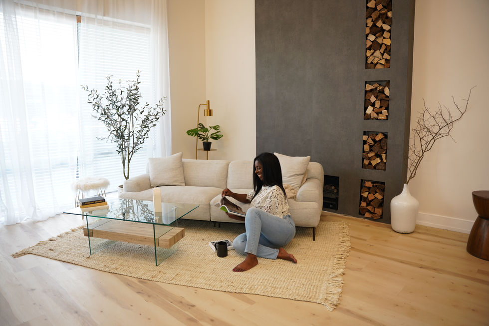 Share Allen reading a book while seated on a cream sofa in a contemporary living room.
