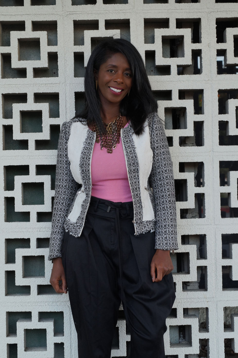 Share Allen walking along a modern building exterior in a pink top and black trousers.