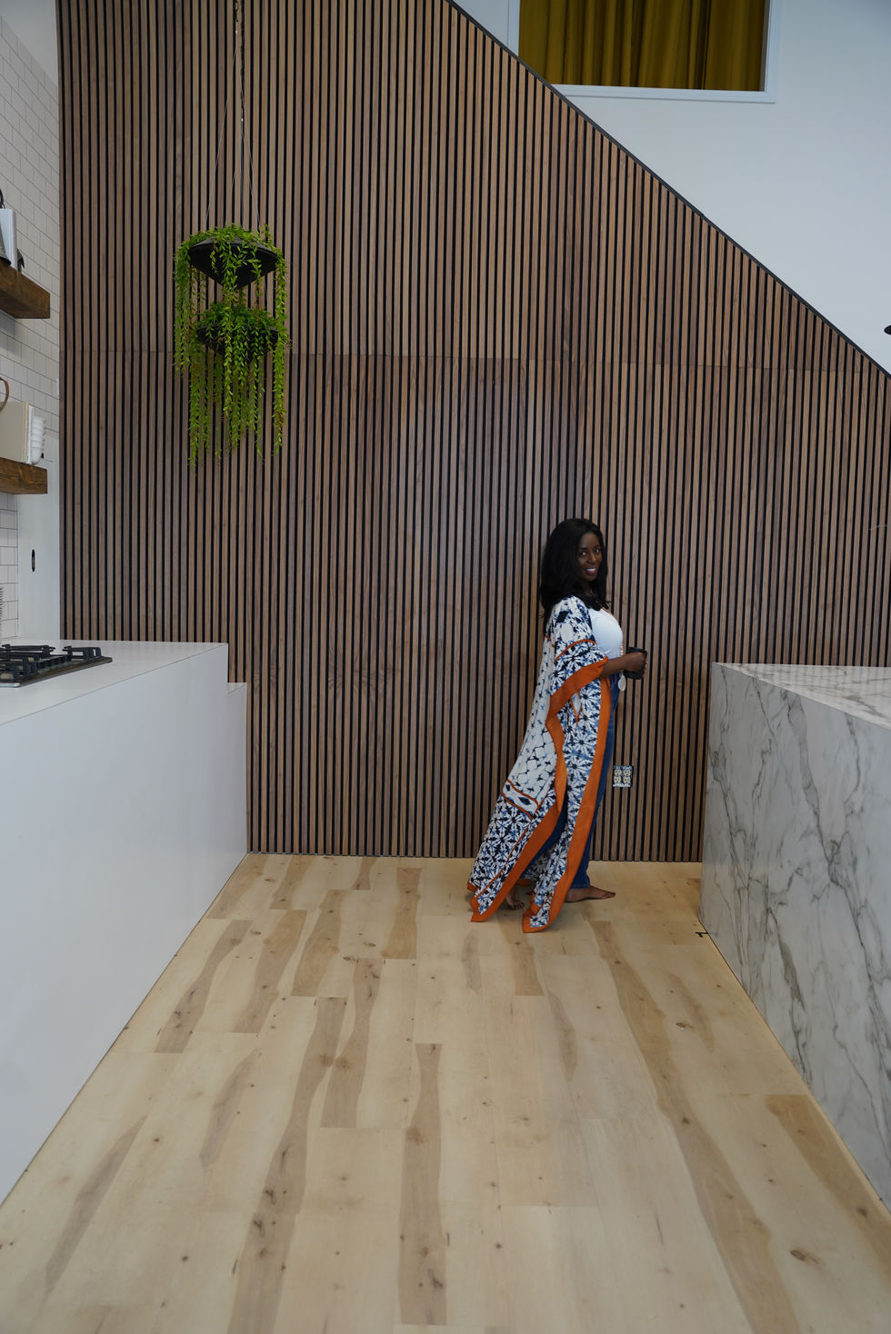 Share Allen standing beside a wood slat wall in a modern kitchen with warm wood floors.