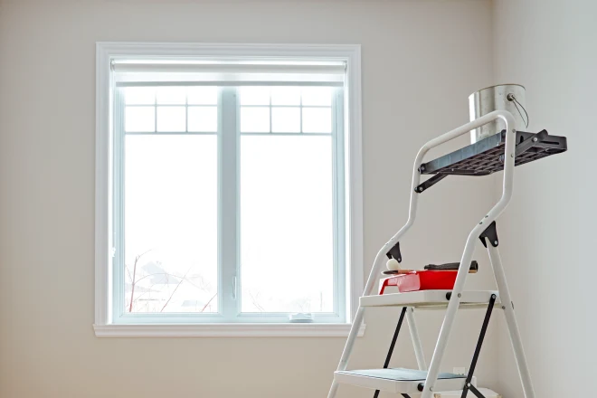 7 Factors that Affect the Cost of Interior Painting 8 A ladder with painting equipment on it in front of a brightly lit window