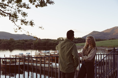 Couple standing on shoreline with Lake District fells at golden hour