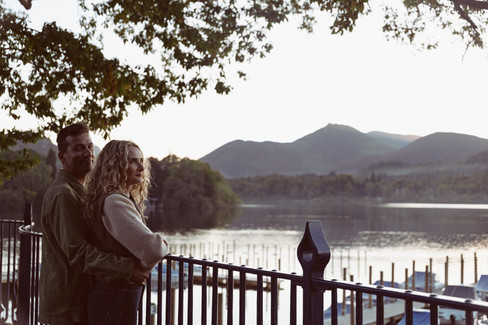Couple standing on shoreline with Lake District fells at golden hour