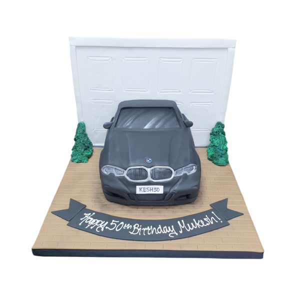 Bespoke cake in Solihull, West Midlands shaped like a BMW 3 Series parked in front of a detailed garage door scene.