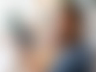 Smiling man in blue shirt holds tablet with graphs at wooden table. Papers, coffee cup nearby. Bright, casual indoor setting.