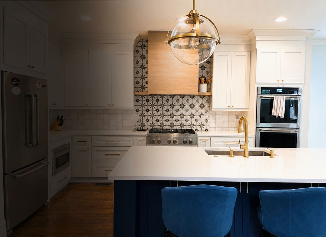Warm, thoughtfully organized kitchen with a white quartz island, white and navy cabinetry, custom white oak hood, brass hardware, built-in appliances, and layered custom storage.