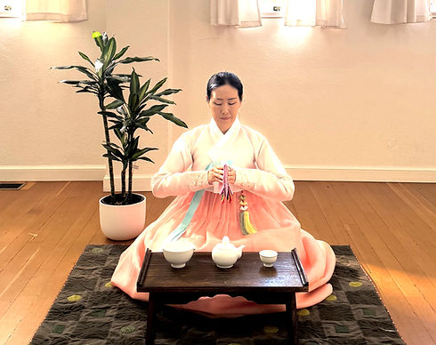 Yuna Lee seated on the floor in traditional Korean hanbok, performing a graceful Korean tea ceremony (Darye) with mindful presence and refined movements in Santa Barbara