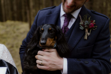 groom holding his dog, wearing a buttonhole on his suit. At his woodland elopement ceremony