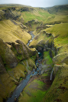 A river flowing at the bottom of a canyon covered in green grass and moss