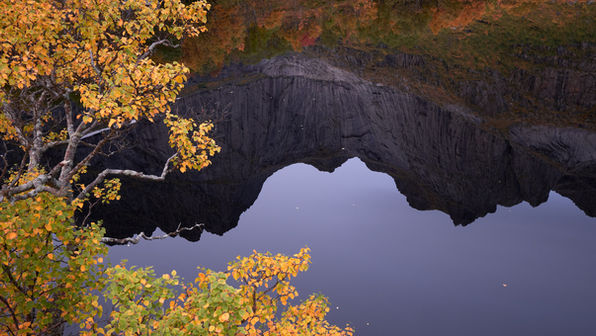 Stjerntinden reflecting in glassy water with autumn colored trees in the foreground