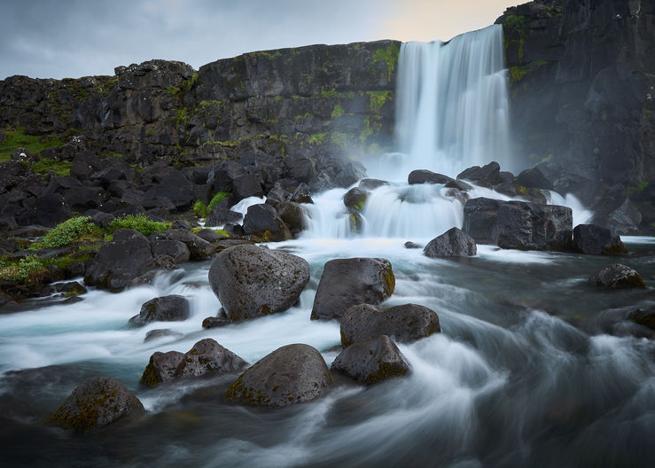 The waterfall Öxararfoss with water flowing around rocks in the foreground