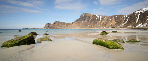 Sand beach with green rocks and mountains in the background in Vesterålen