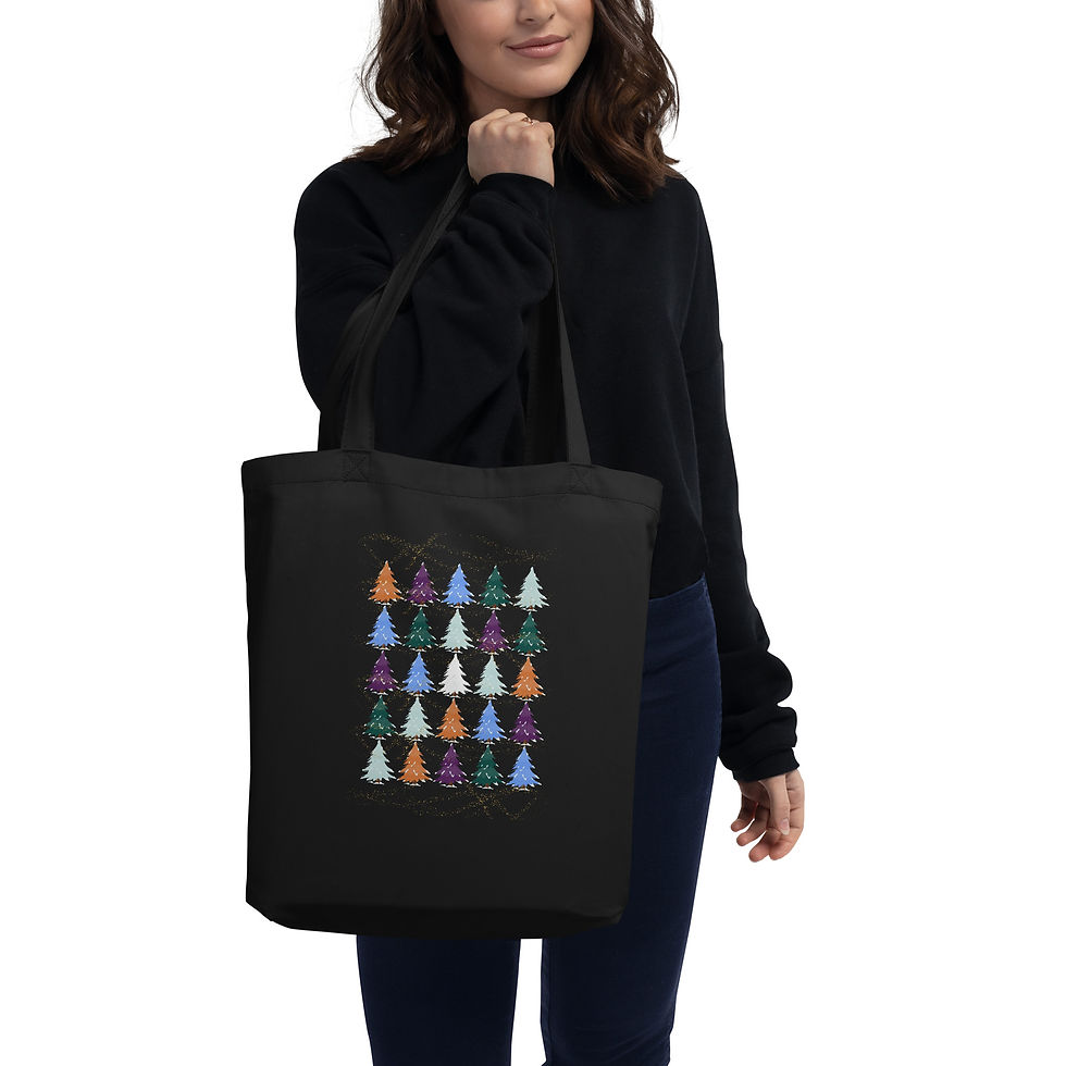 Woman holding a black tote bag featuring colorful Christmas trees pattern. She wears a black sweater, standing against a plain white background.