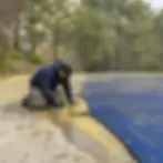 Scrubbing pollen stains off a concrete pool deck next to a covered pool in Elkton