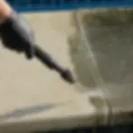 Close-up hand cleaning algae-stained pool coping with surface cleaner wand
