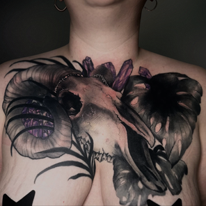Black and grey animal skull chest tattoo with floral and crystal details across the chest.