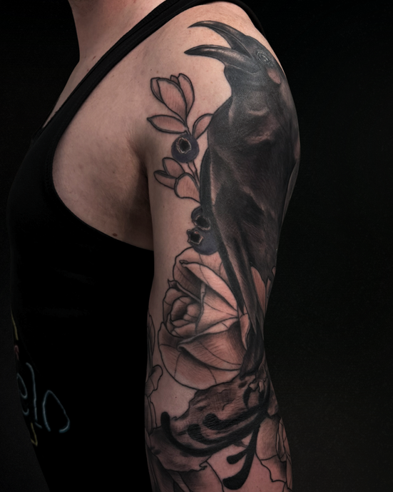 Floral with raven blackout shoulder tattoo with layered petals and blackwork.