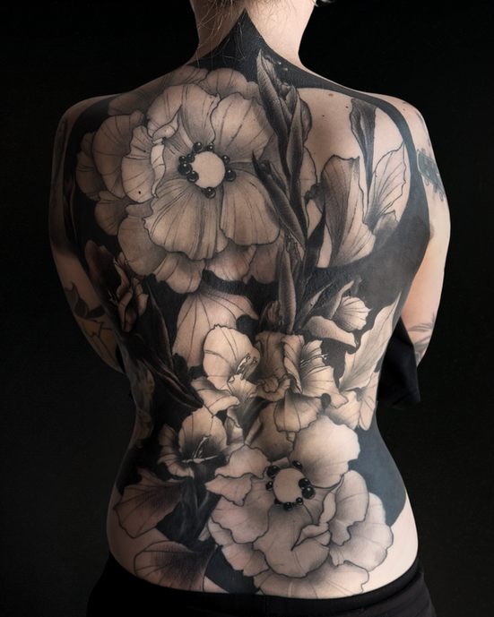 Large floral back tattoo in black and grey covering the upper back.