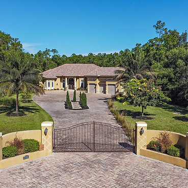 Wide-angle front exterior view of a private gated luxury estate in Naples, Florida, featuring a grand wrought-iron security g