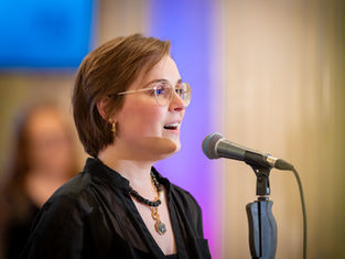 A close up photograph of Rachael Heater, wearing a black top, singing in Parliament Buildings.