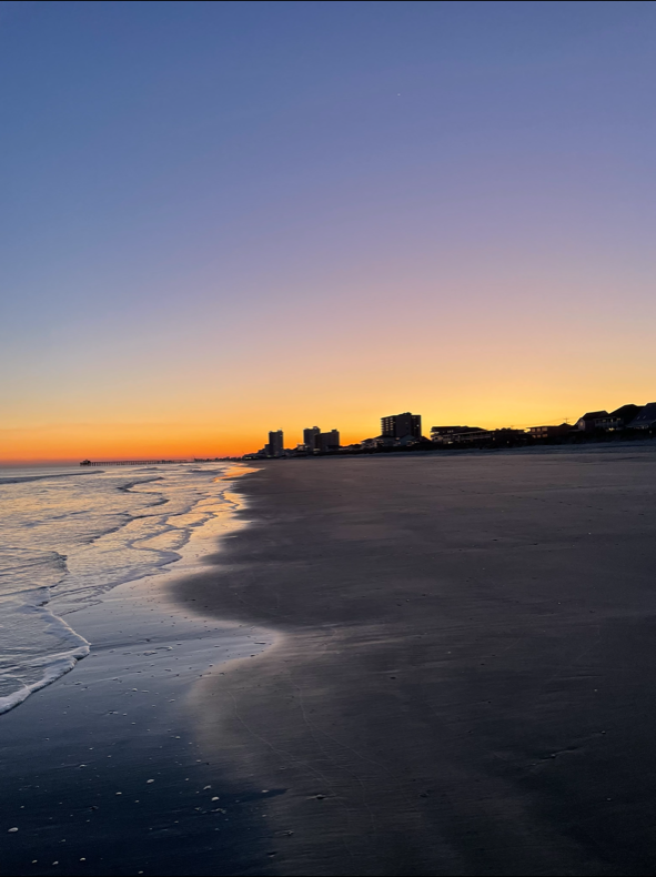 Picture of a beach at sunset with buildings in the horizon 