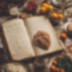 Open cookbook with handwritten recipes, surrounded by bread, tomatoes, and a glass of beer, on a rustic wooden table setting. Warm tones.