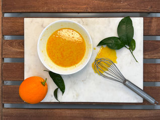 an orange glaze in a bowl with an orange and a whisk on the sides