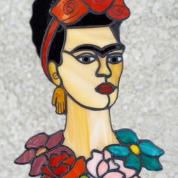 A stained glass portrait of Frida Kahlo, with a collar of various flowers.