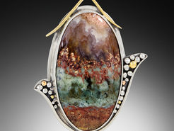 A shiny, ovular stone pendant with green and brown hues in a decorated silver and gold frame.