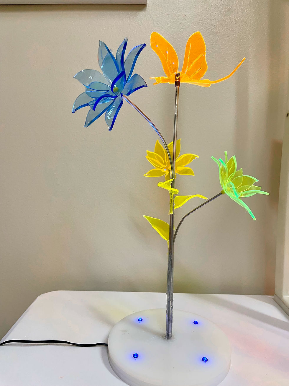 A metal-stemmed sculpture of several flowers and a butterfly in bright, translucent colors.