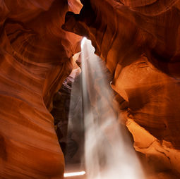 The inside of a rocky orange cave, bathed in bright light.