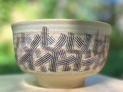 A white and tan pottery vessel carved with interlocking patterned lines.